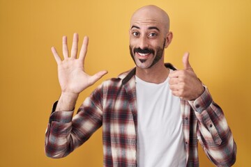 Hispanic man with beard standing over yellow background showing and pointing up with fingers number six while smiling confident and happy.