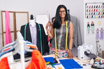 Middle age hispanic woman tailor smiling confident cutting cloth at tailor shop