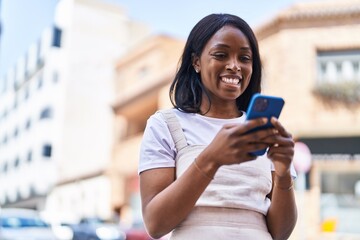 Fototapeta premium Young african american woman smiling confident using smartphone at street