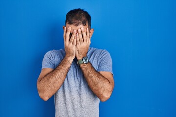 Middle east man with beard standing over blue background with sad expression covering face with...