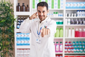 Handsome hispanic man working at pharmacy drugstore smiling doing talking on the telephone gesture...