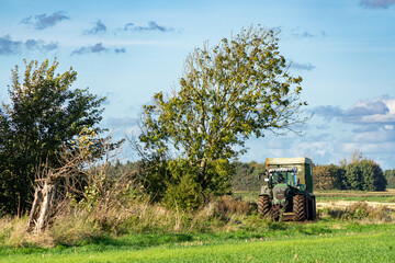 Obraz premium Tractor driving into the shadow of a windbent tree in an idyllic rural surrounding