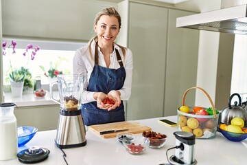Young blonde woman smiling confident holding raspberries at kitchen