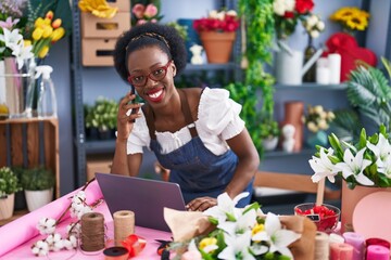 African american woman florist talking on smartphone using laptop at florist store