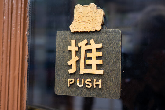 Close up of a door hanger at a Japanese restaurant. Japanese character for "push". Press to open. Wooden sign with a cat.