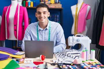 Young hispanic man tailor using laptop at sewing studio