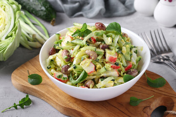 Salad with cabbage, crab sticks, beans, eggs and cucumber in white bowl on wooden board © Anzhela