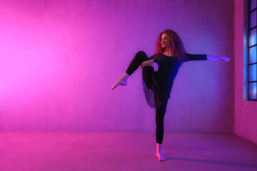 Fototapeta na wymiar Modern dance girl dancer dancing in neon light doing gymnastic exercises in studio, copy space.