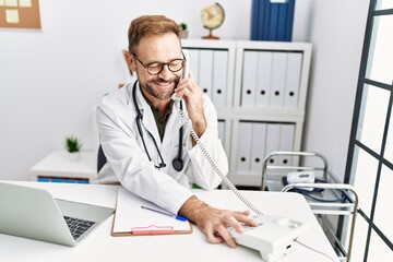 Middle age hispanic man wearing doctor uniform talking on the telephone at clinic