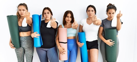 Group of women holding yoga mat standing over isolated background showing middle finger, impolite...