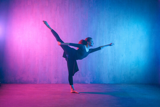 Modern dance girl dancer dancing in neon light doing gymnastic exercises in studio, copy space.