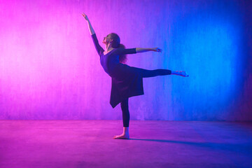 Modern dance girl dancer dancing in neon light doing gymnastic exercises in studio, copy space.