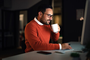 Businessman working overtime at the office, drinking coffee, and working online.