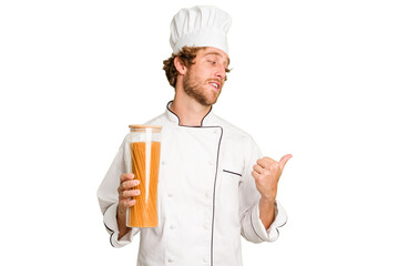 Young cook man isolated on white background points with thumb finger away, laughing and carefree.