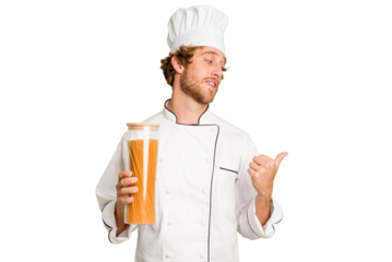 Young cook man isolated on white background points with thumb finger away, laughing and carefree.