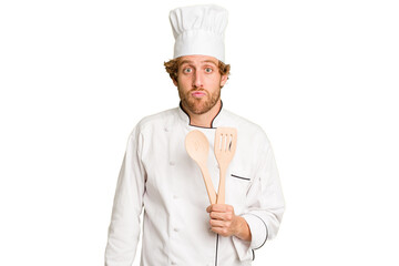 Young cook man isolated on white background shrugs shoulders and open eyes confused.