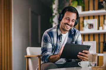 Happy man using a digital tablet, smiling and using headphones, listening to the music.