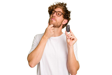 Young caucasian man holding car keys isolated on white background looking sideways with doubtful...