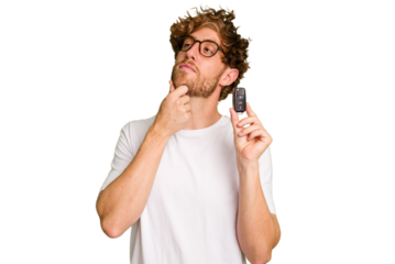 Young caucasian man holding car keys isolated on white background looking sideways with doubtful and skeptical expression.