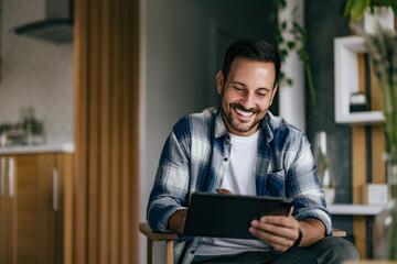 Smiling man enjoying at home, using a digital tablet.