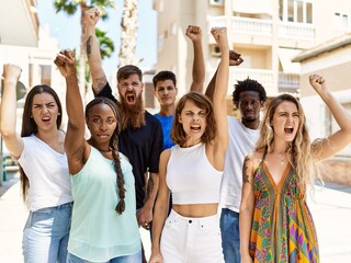 Group of young activists protesting with fists raised up standing at the city.