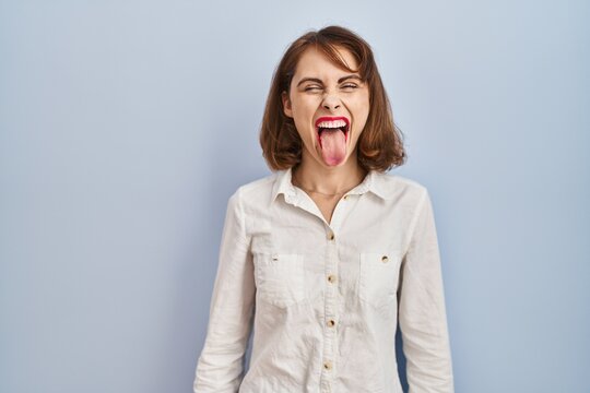 Young beautiful woman standing casual over blue background sticking tongue out happy with funny expression. emotion concept.