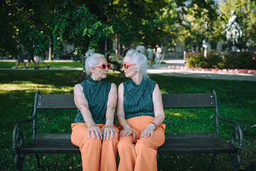Happy senior sister, twins sitting in city park and resting after shopping. - obrazy, fototapety, plakaty