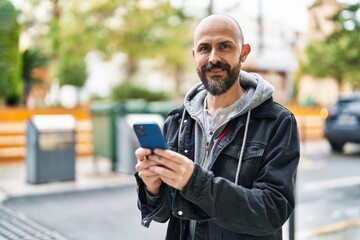 Obraz premium Young bald man smiling confident using smartphone at street