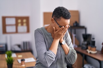 African american woman working at the office wearing glasses with sad expression covering face with...