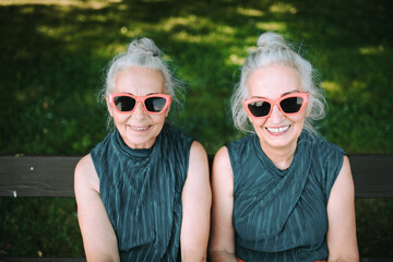 High angle view of happy senior women, twins in same clothes, smiling and posing in city park. - obrazy, fototapety, plakaty