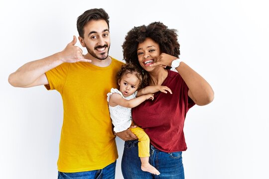 Interracial Young Family Of Black Mother And Hispanic Father With Daughter Smiling Doing Phone Gesture With Hand And Fingers Like Talking On The Telephone. Communicating Concepts.