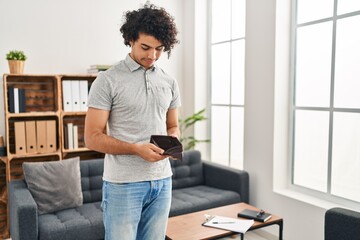 Young hispanic man showing empty wallet standing at home
