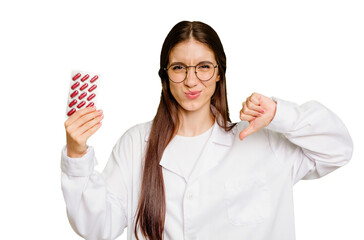 Young pharmacist woman holding a tablet of pills isolated showing a dislike gesture, thumbs down....