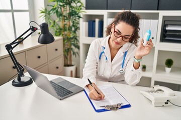 Young beautiful hispanic woman doctor holding nasal treatment writing on document at clinic