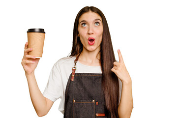 Young barista woman holding a takeaway coffee isolated pointing upside with opened mouth.