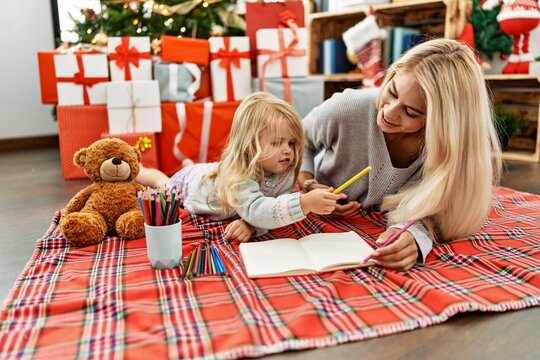 Mother and daughter drawing on notebook lying by christmas tree at home