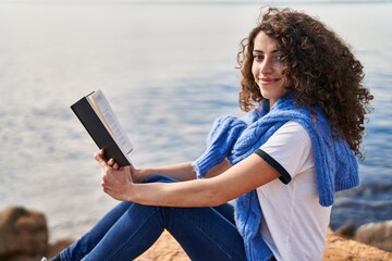 Young hispanic woman smiling confident reading book at seaside