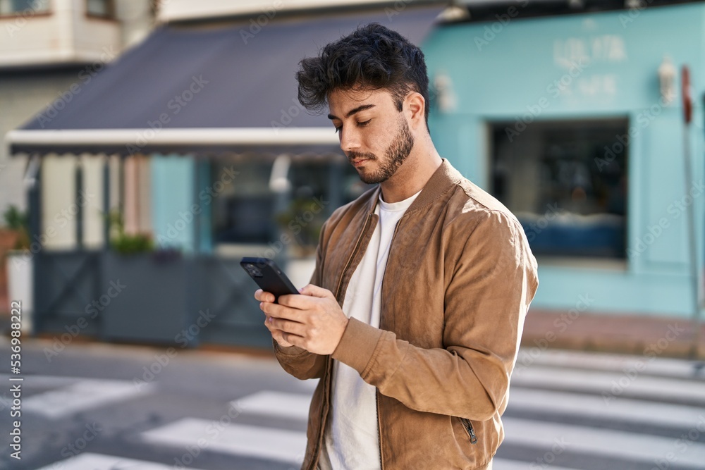 Poster Young hispanic man using smartphone at street