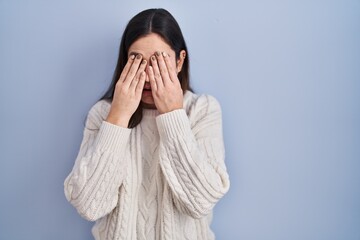 Young brunette woman standing over blue background rubbing eyes for fatigue and headache, sleepy and tired expression. vision problem