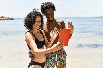 Young interracial tourist couple having video call using touchpad at the beach.