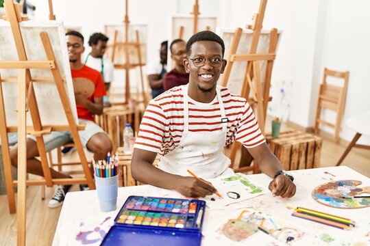 Young african man at art studio looking positive and happy standing and smiling with a confident smile showing teeth