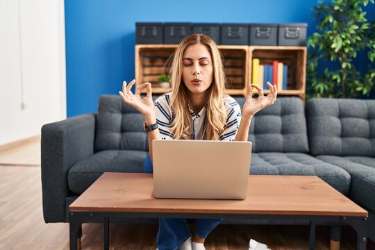 Young blonde woman having online yoga class sitting on sofa at home