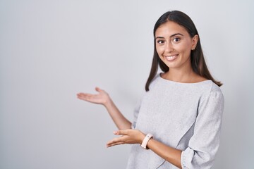 Young hispanic woman standing over white background inviting to enter smiling natural with open hand
