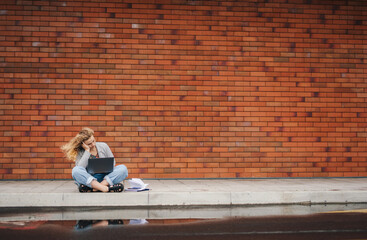 Portrait of happy woman student holding and working on laptop while sitting at the urban street. Urban leisure concept. Searches the Internet. The concept of a