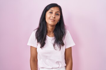 Fototapeta premium Young hispanic woman standing over pink background relaxed with serious expression on face. simple and natural looking at the camera.