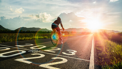New year 2023 or start straight and beginning concept.Blurry Man ride on bike and word 2023 start written on the road at sunset add lens flare.Concept of challenge or career path,business strategy.