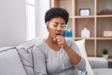 Young african american woman wearing virtual reality glasses sitting on the sofa feeling unwell and coughing as symptom for cold or bronchitis. health care concept.
