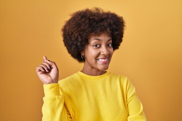 Fototapeta na wymiar Young african american woman standing over yellow background with a big smile on face, pointing with hand and finger to the side looking at the camera.