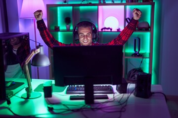 Young caucasian man streamer playing video game with winner expression at gaming room