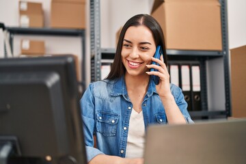 Young beautiful hispanic woman ecommerce business worker using laptop talking on smartphone at office